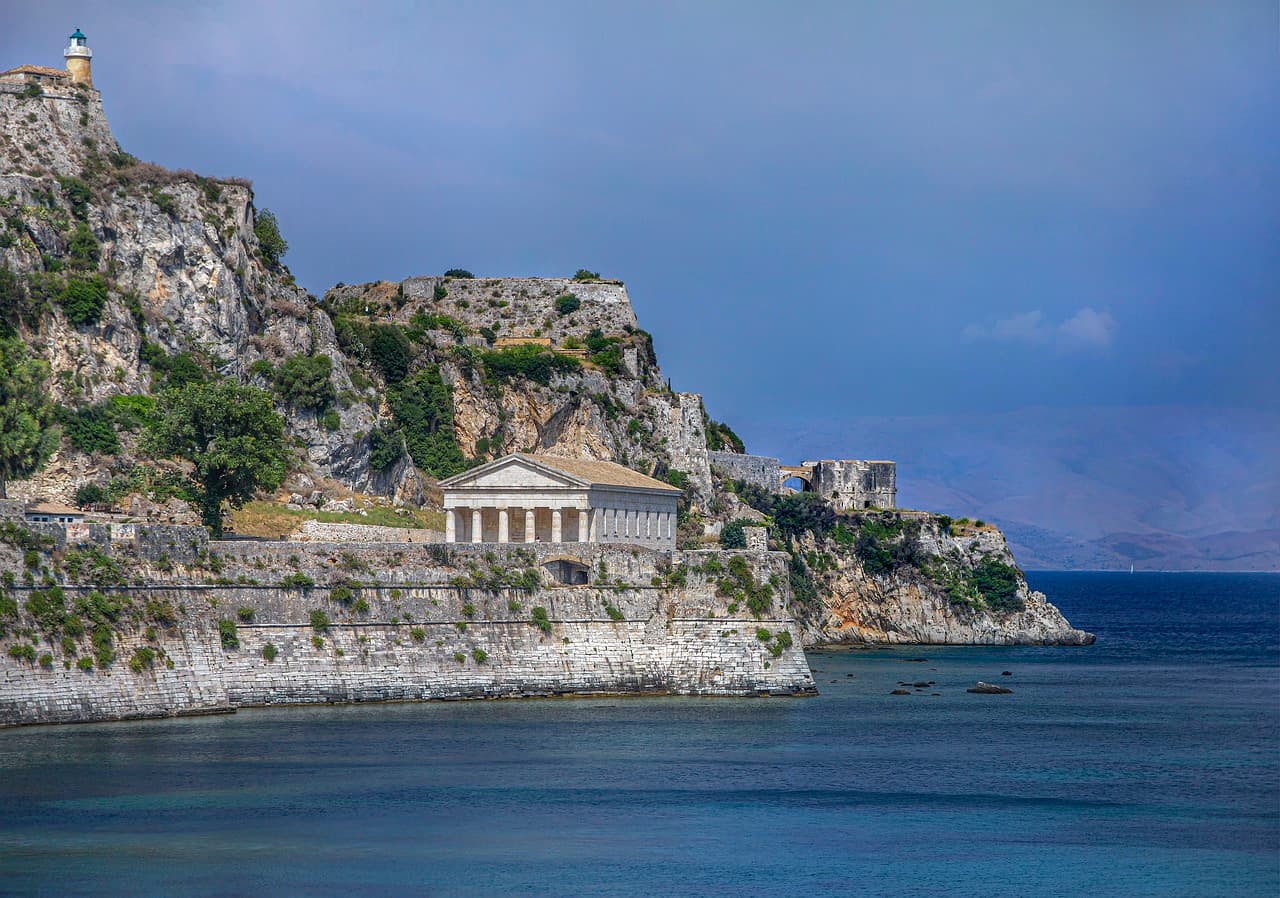 Un temple grec sur une falaise au-dessus d'une eau azure.