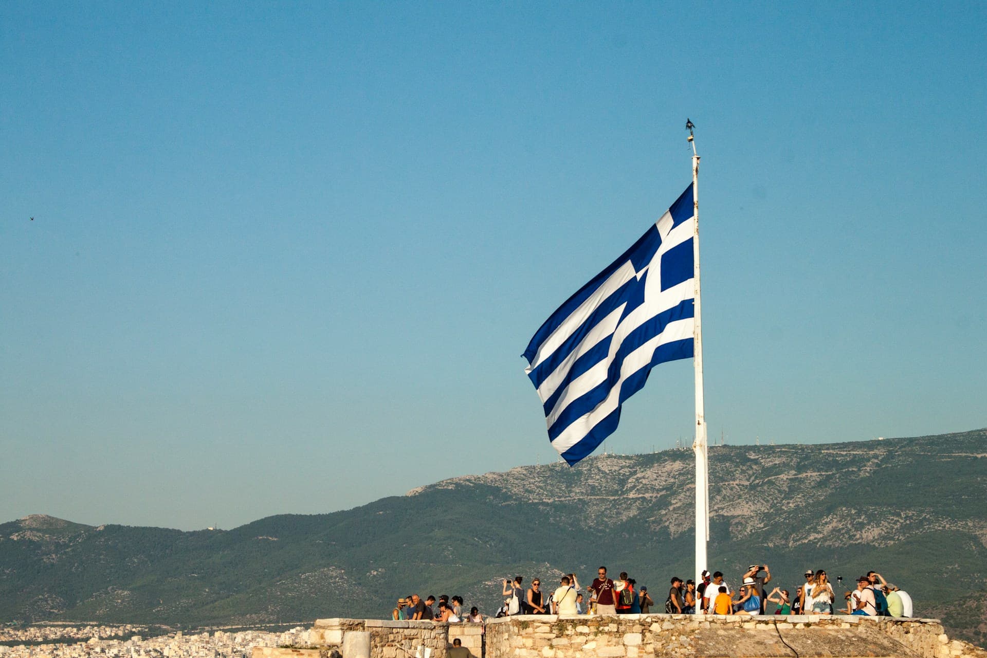 Η ελληνική σημαία κυματίζει στον καθαρό γαλάζιο ουρανό με μπλε και λευκά χρώματα.