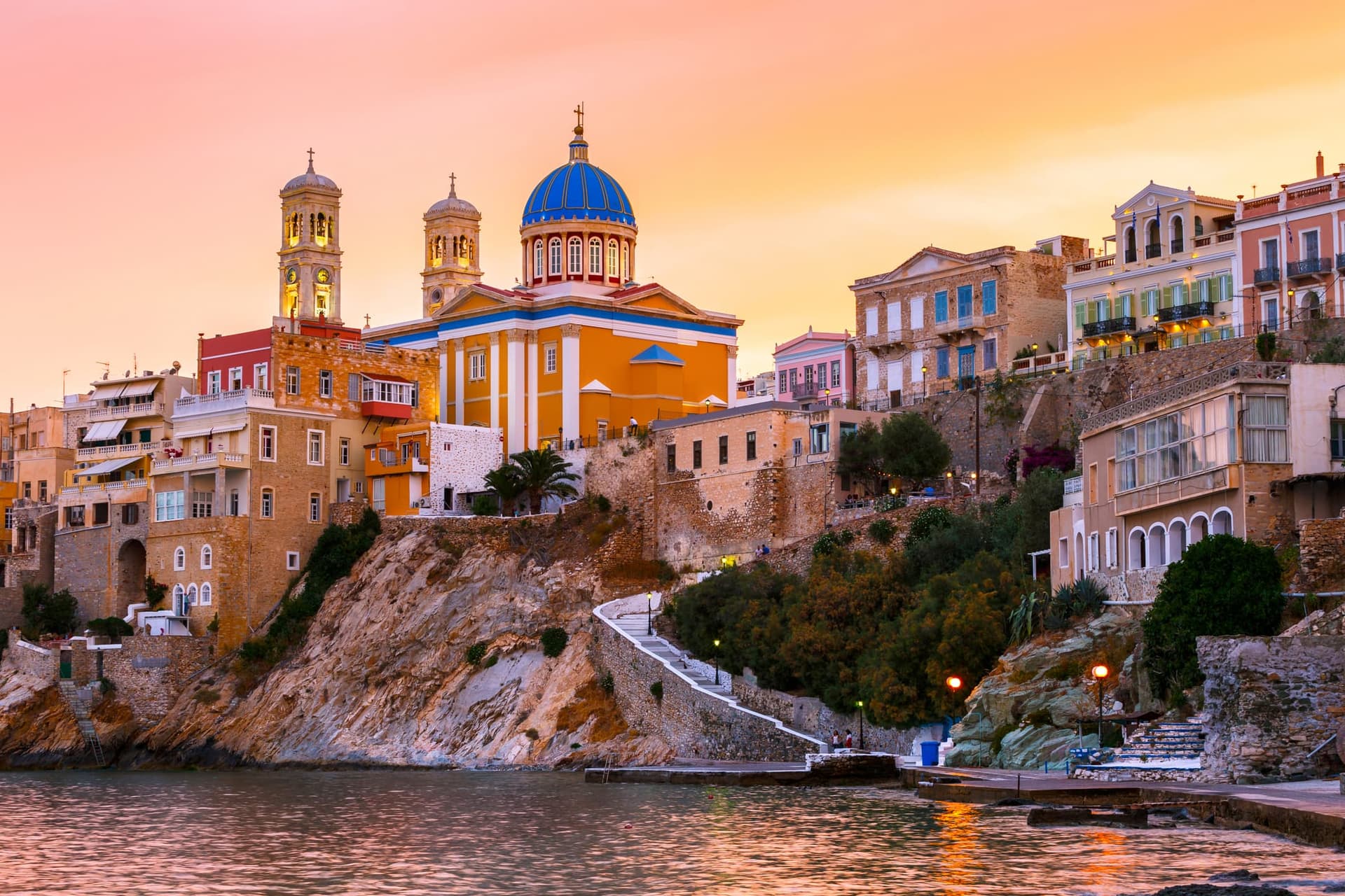 Πανοραμική θέα των Βαποριών στη Σύρο με το εντυπωσιακό μπλε τρούλο της εκκλησίας και τα νεοκλασικά σπίτια στο ηλιοβασίλεμα.