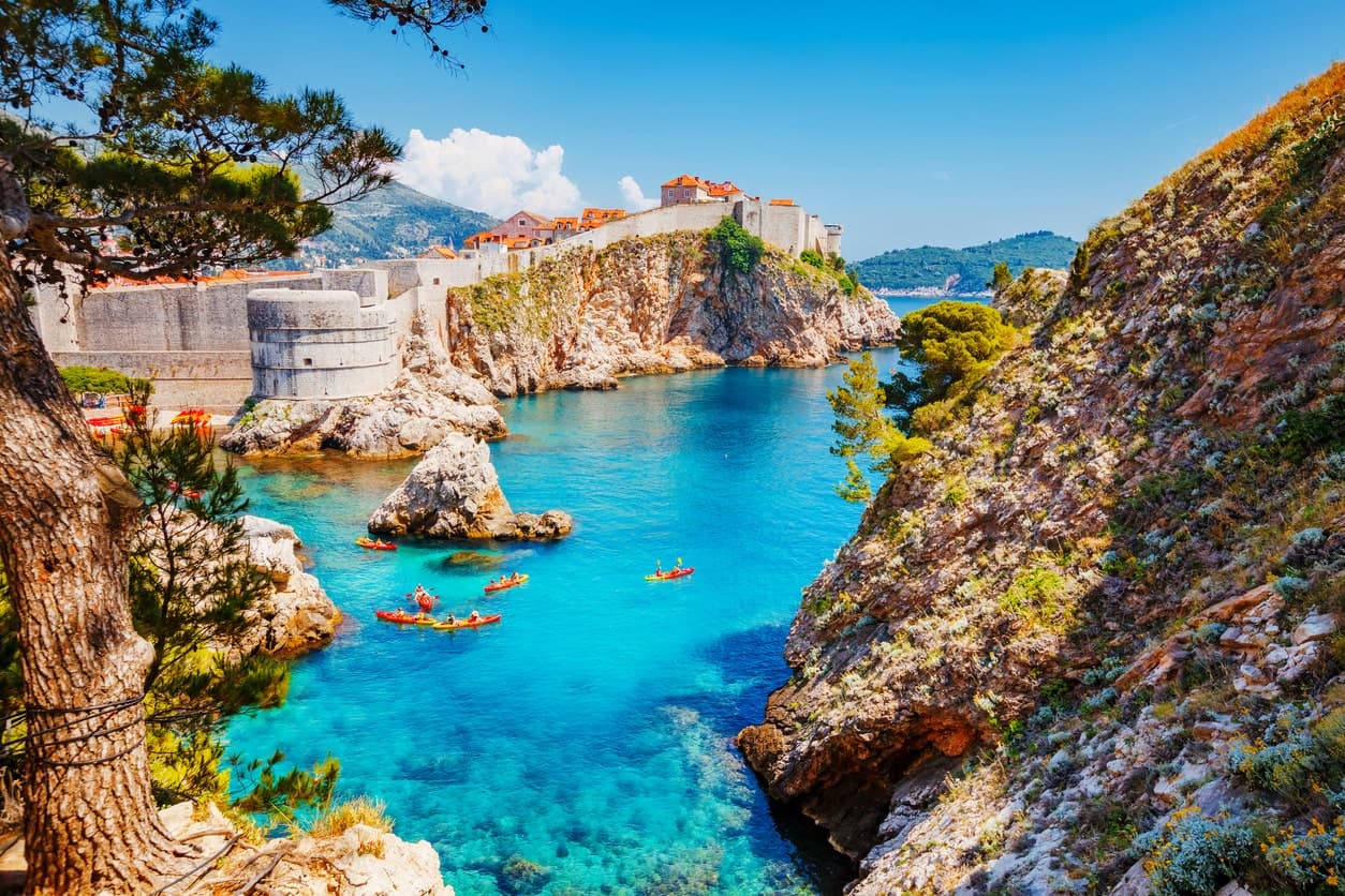 Blick auf die Altstadtmauer von Dubrovnik, Kroatien, mit türkisblauem Meer und Kajakfahrern