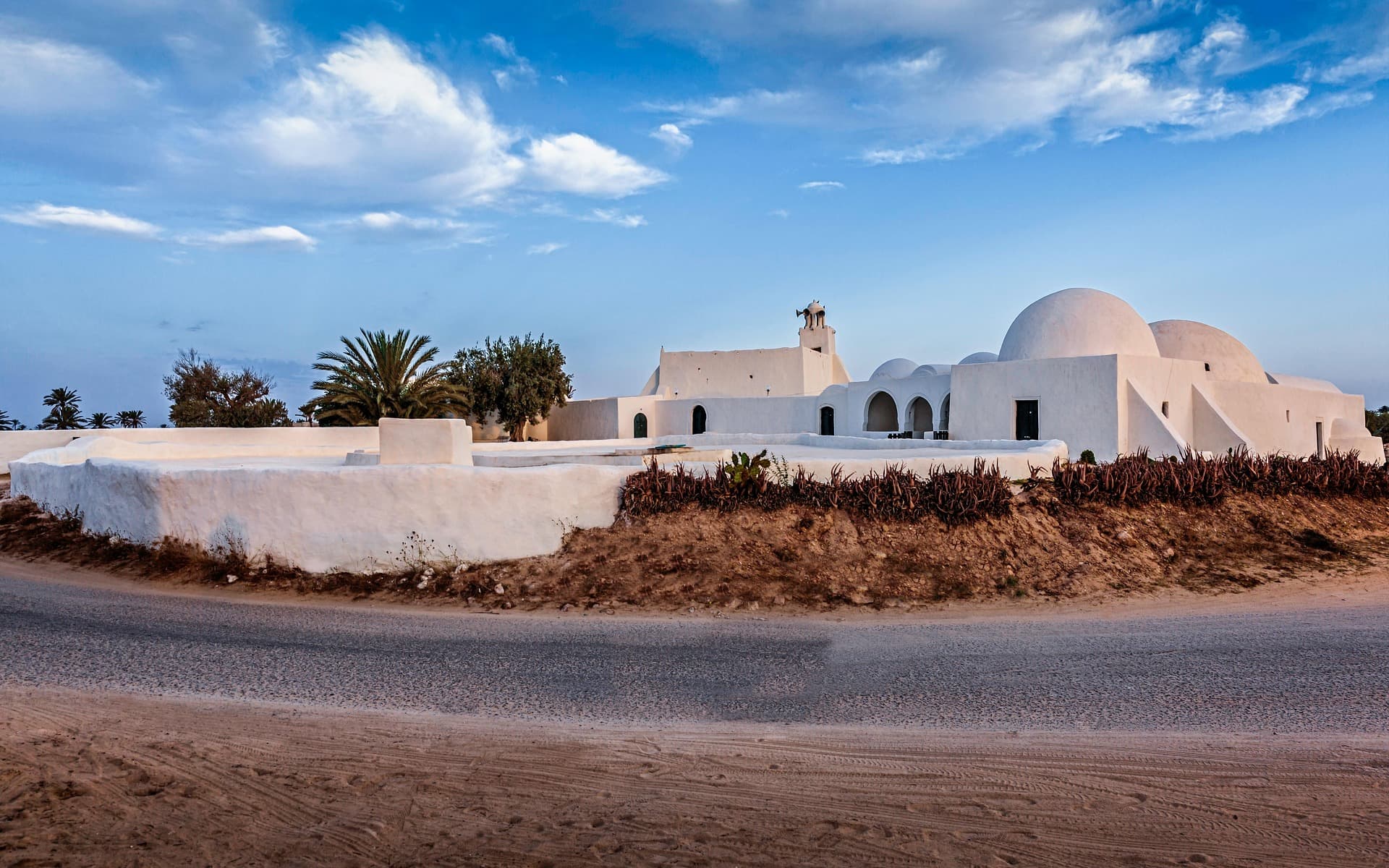 A dazzling white mosque by the beach under a sunset.