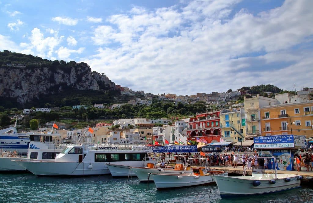 Veduta di Marina Grande a Capri con le case colorate affacciate sul porto, barche ormeggiate e mare calmo sotto un cielo luminoso.