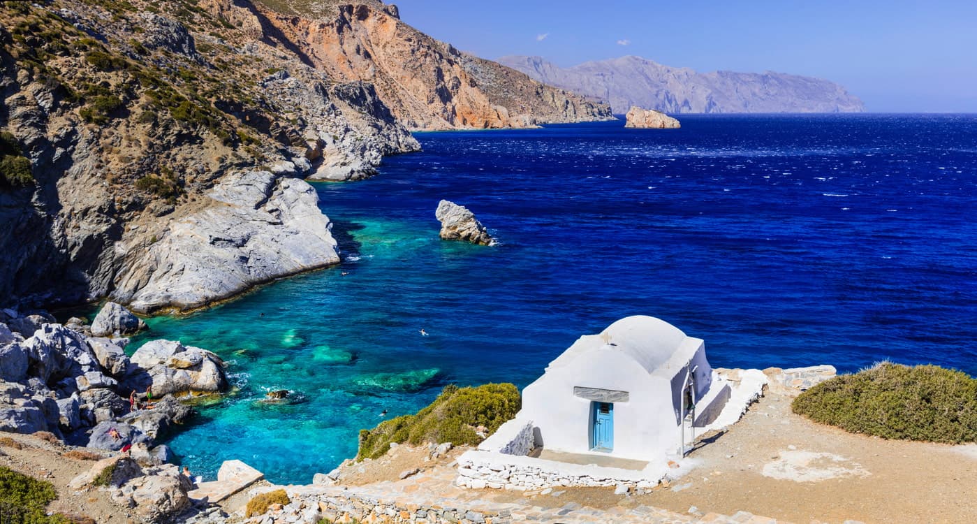 Une petite crique grecque à l'eau bleue et profonde, avec une petite chapelle blanche sur le bord