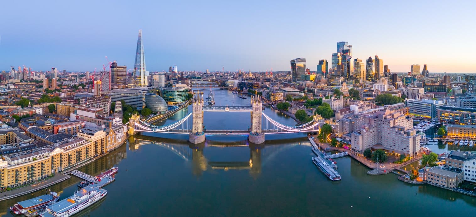 Vue aérienne de Londres avec le Tower Bridge illuminé et la ligne d'horizon au coucher du soleil.