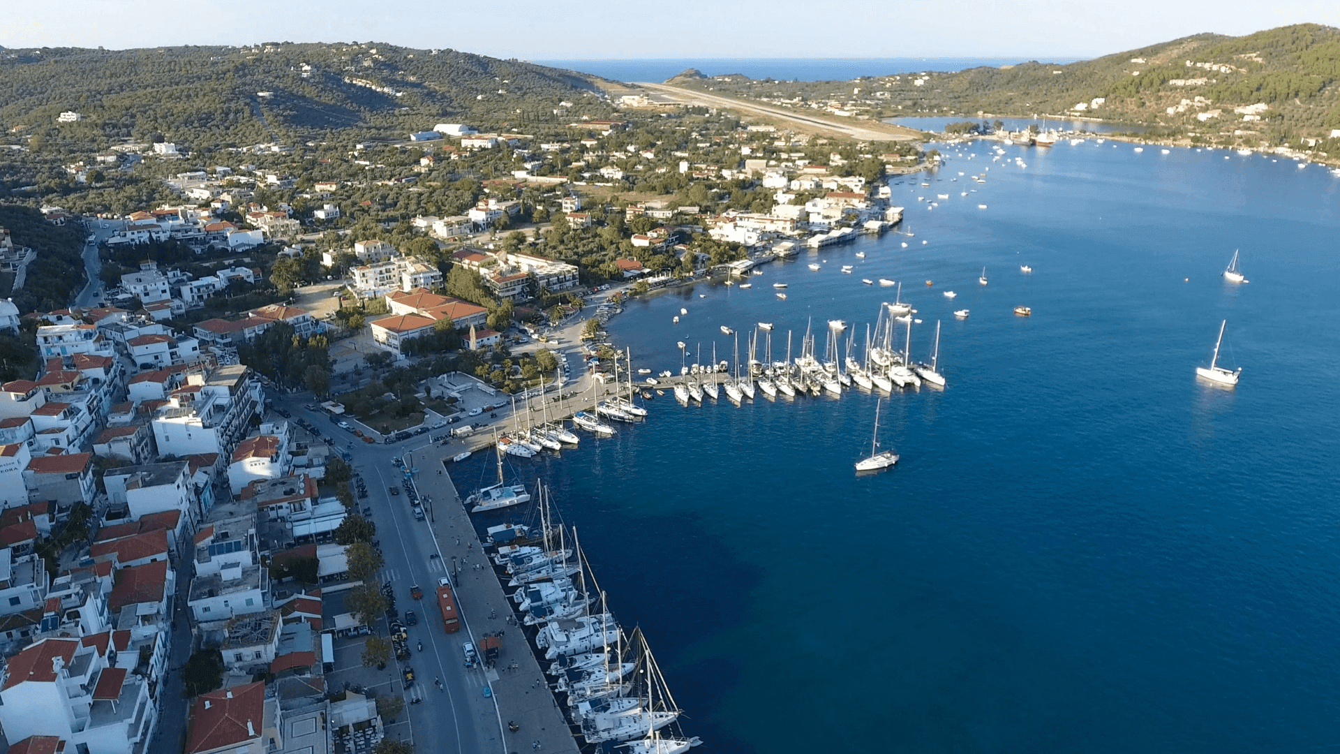 το λιμανι της Σκιαθου με πολλα καραβια και κτιρια με κοκκινες σκεπες αναμεσα στην πλουσια βλαστιση