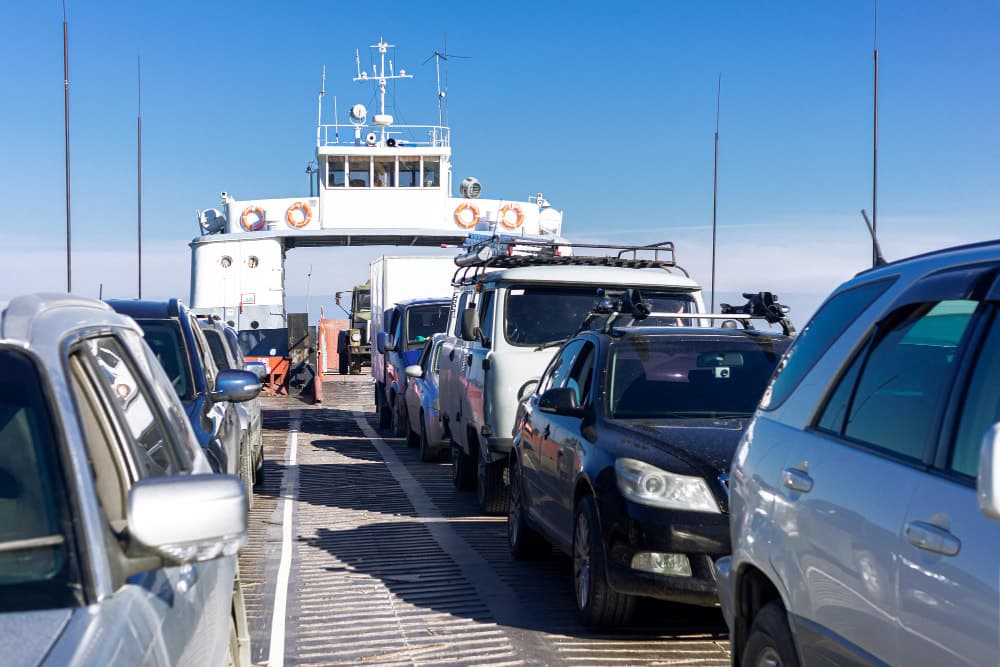 Des voitures alignées sur le pont d'un ferry, prêtes à être transportées à travers un plan d'eau.