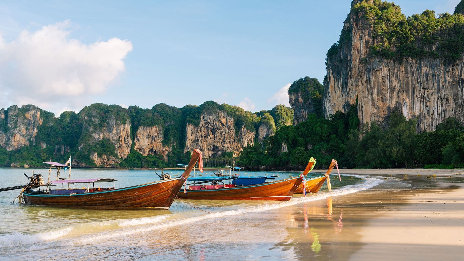 Two small fishing boats are docked on the pristine white shores of Krabi, Thailand.